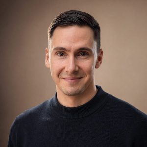 Portrait von Dr. Johannes Christoph im blaunen Pullover vor beigem Studiohintergrund