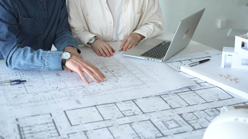Architekturbüro bei einer Planbesprechung mit Bauplänen und Laptop zum Thema SEO für Architekten.